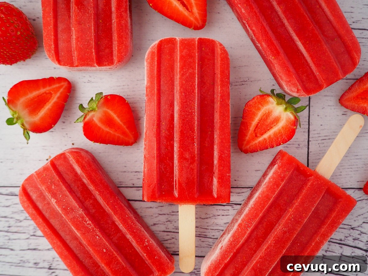 Close up of a strawberry popsicle, surrounded by fresh strawberries and other strawberry popsicles.