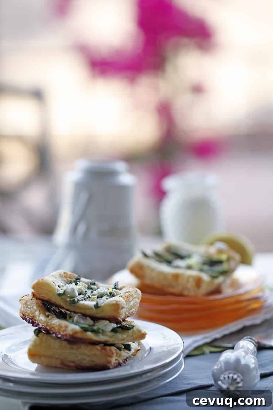 A plate of pastries, including an Asparagus Ricotta Puff Pastry Tart, on a table next to a cup of tea.