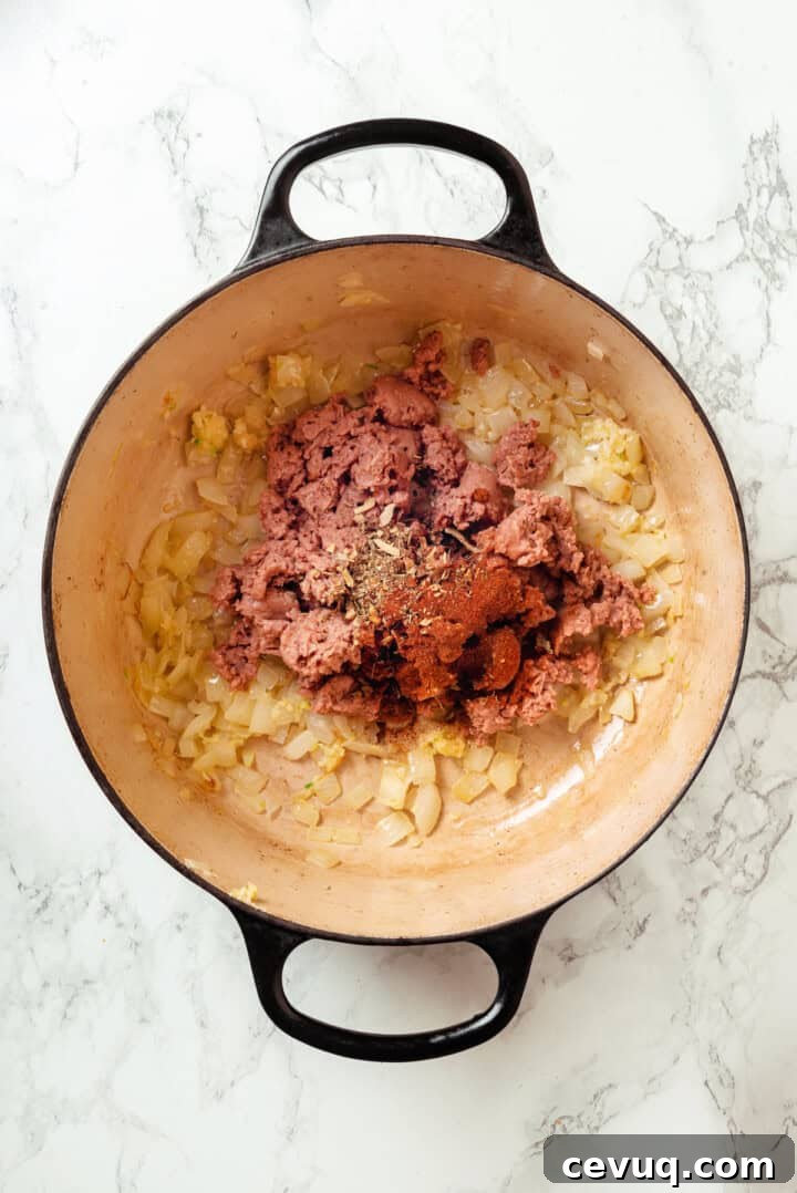 Seasonings and vegan sausage added to pot of sauteed onions