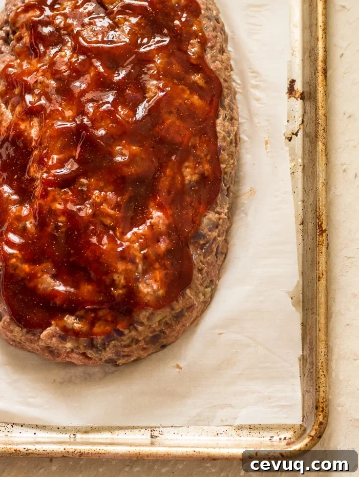 A raw meatloaf with brown sugar ketchup glaze on a parchment lined cookie sheet