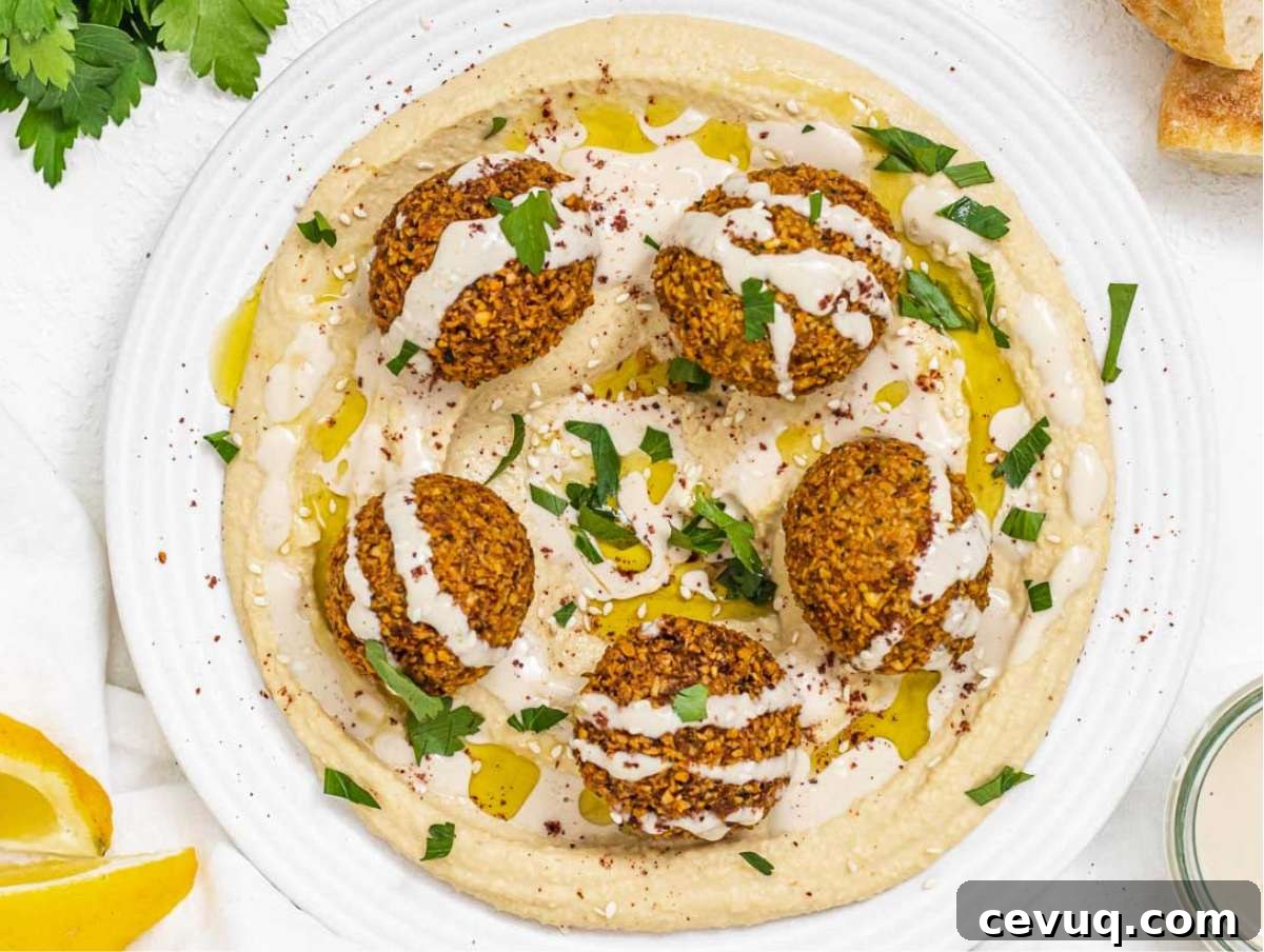 Falafel served on a bed or hummus, topped with tahini sauce, parsley, and sumac.