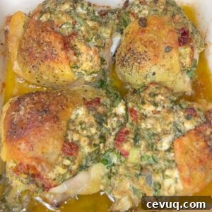 Four baked chicken thighs topped with a mixture of herbs, cheese, and seasonings, sitting in a pan with golden juices and a crispy, browned skin.