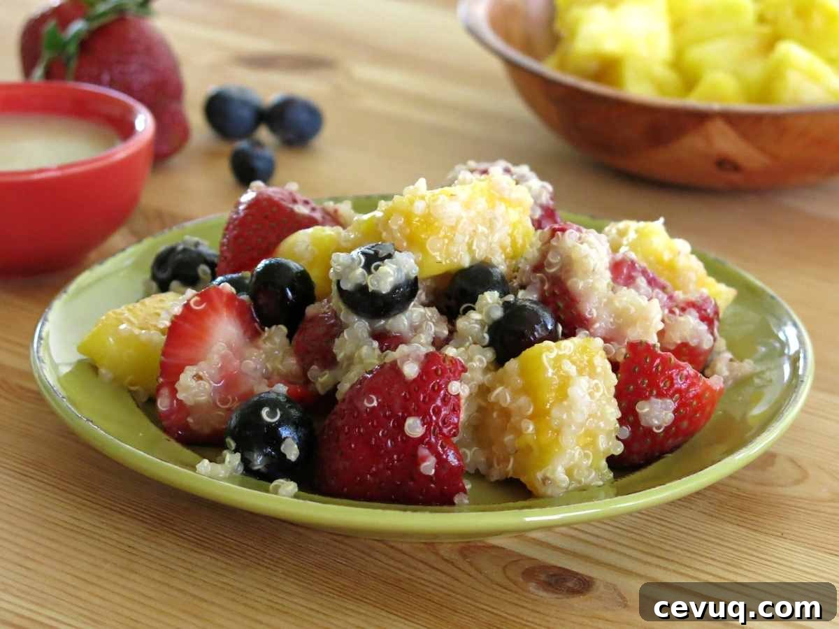 Serving of quinoa fruit salad on a plate with honey lime dressing and fruit in the background.