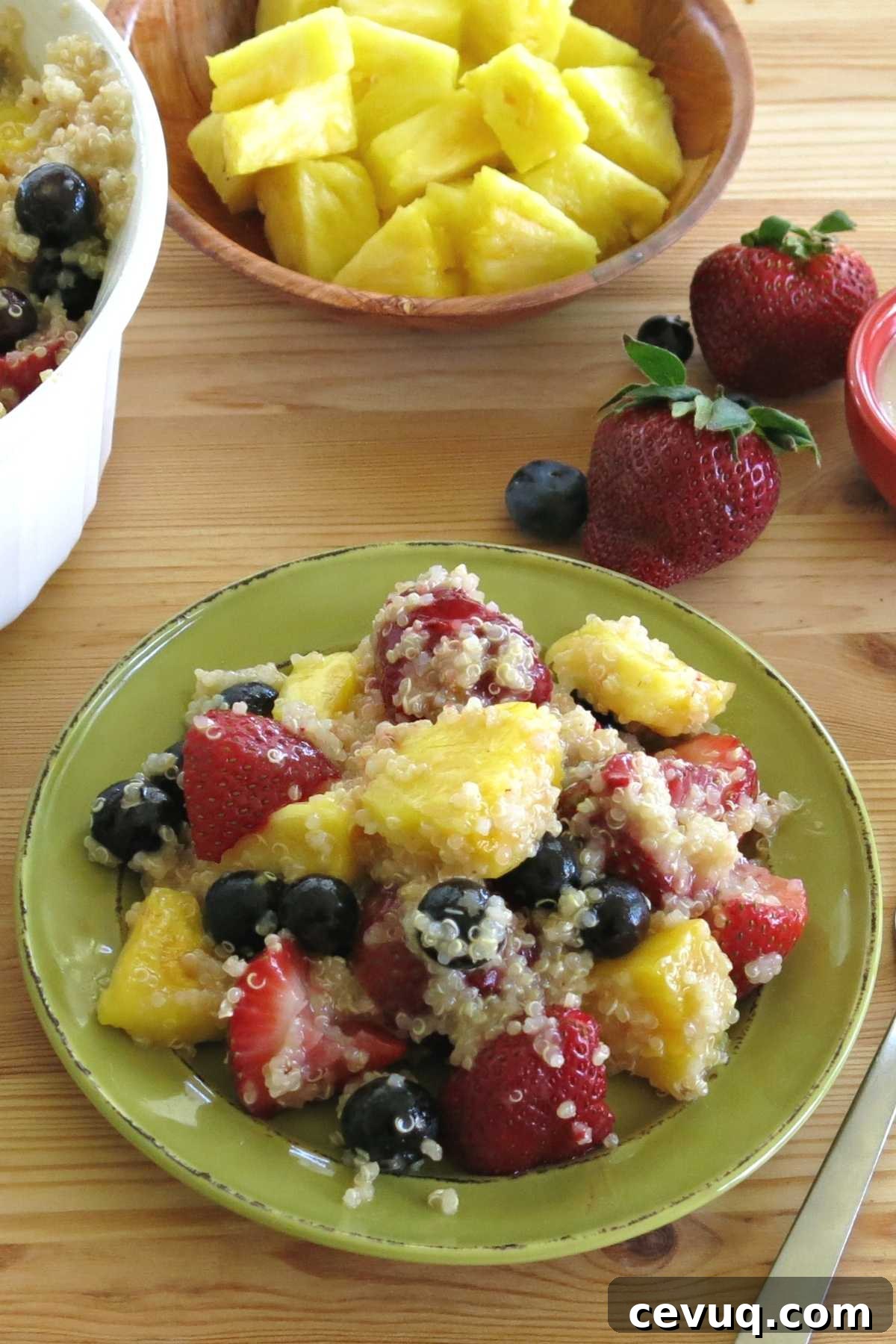 Fruit salad with blueberries, strawberries, pineapple, and quinoa on a plate with ingredients in the background.