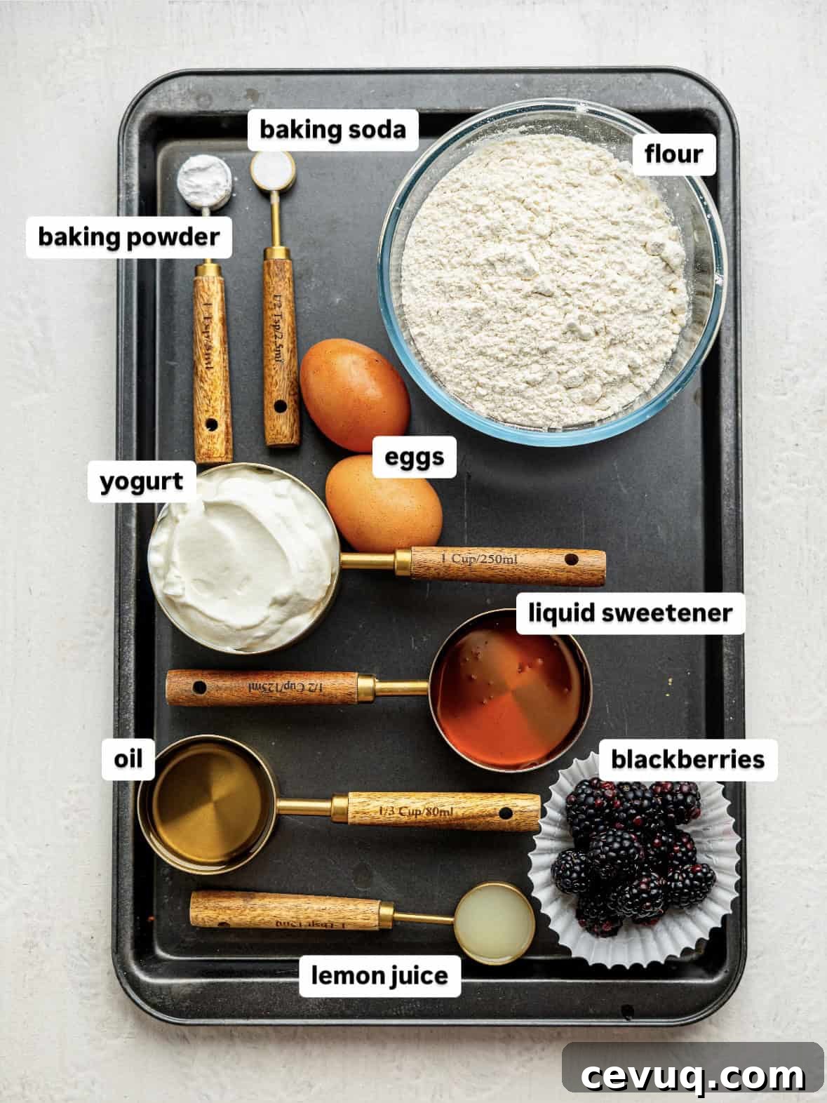 Ingredients for gluten-free blackberry muffins in measuring cups on a baking tray.