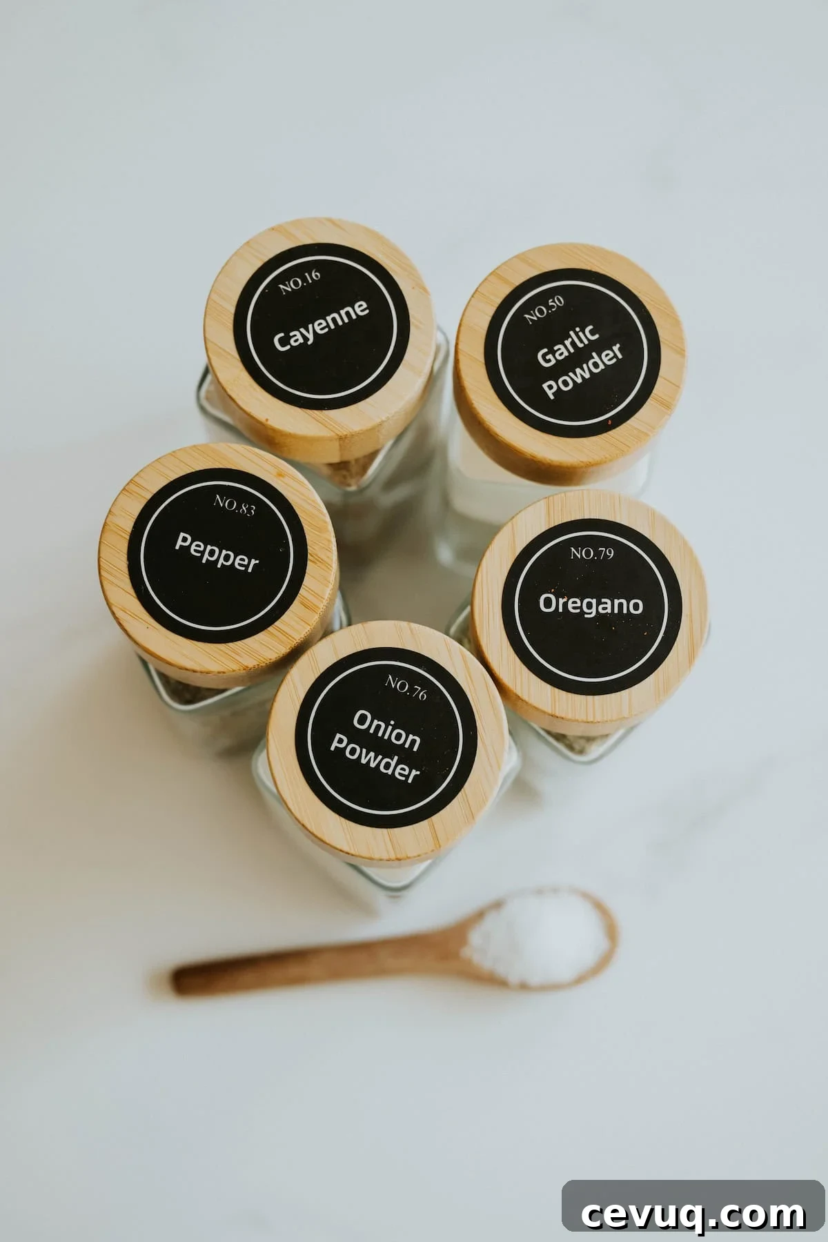 A group of spice jars labeled with seasonings stacked together with a measuring spoon on white marble.