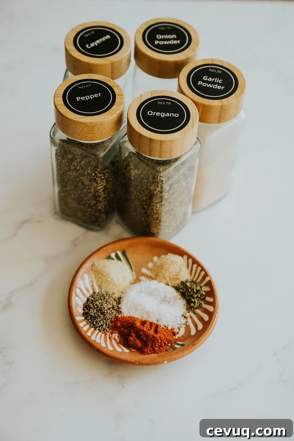 Small jars of spices labeled with black lids next to a plate of measured spices on a marble surface.