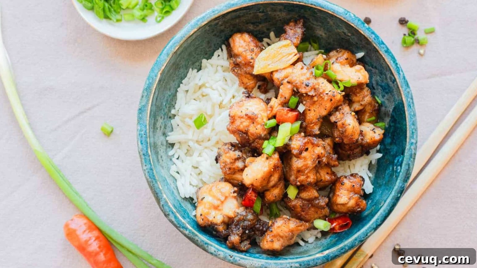 A bowl of white rice topped with stir-fried chicken pieces and chopped green onions, with chopsticks beside it.