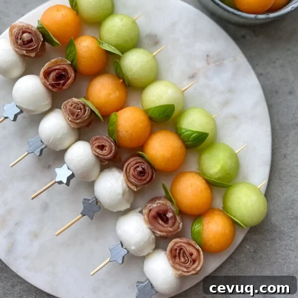 Skewers with mozzarella balls, rolled prosciutto, green and orange melon balls, and fresh basil leaves, arranged neatly on a round marble platter—perfect for healthy bites or inspiring new food recipes.