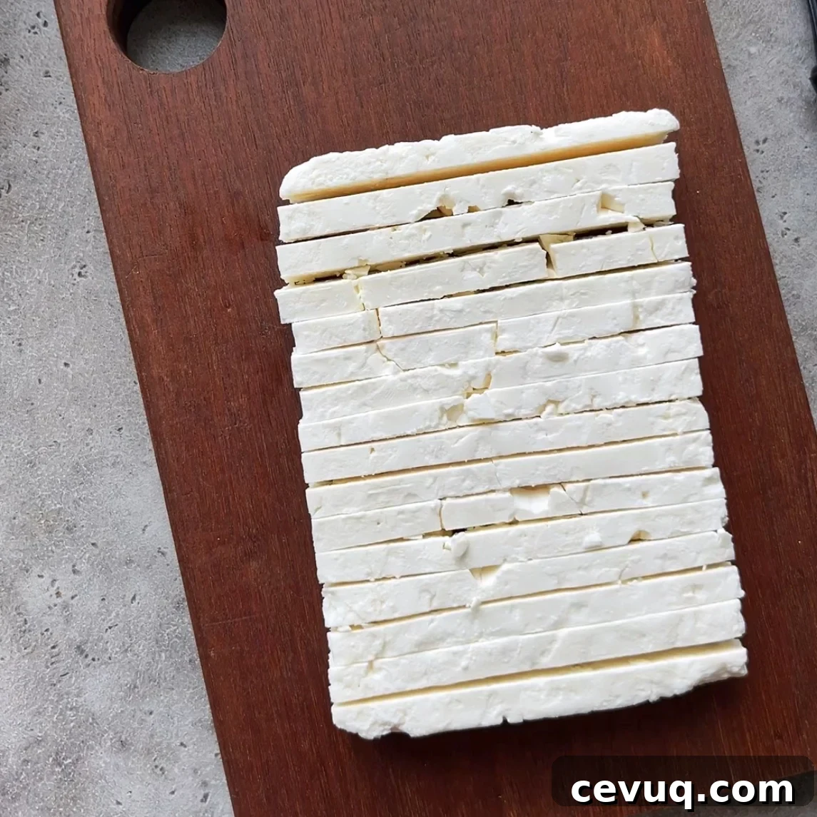 A block of white feta is evenly sliced and placed on a rectangular wooden cutting board.