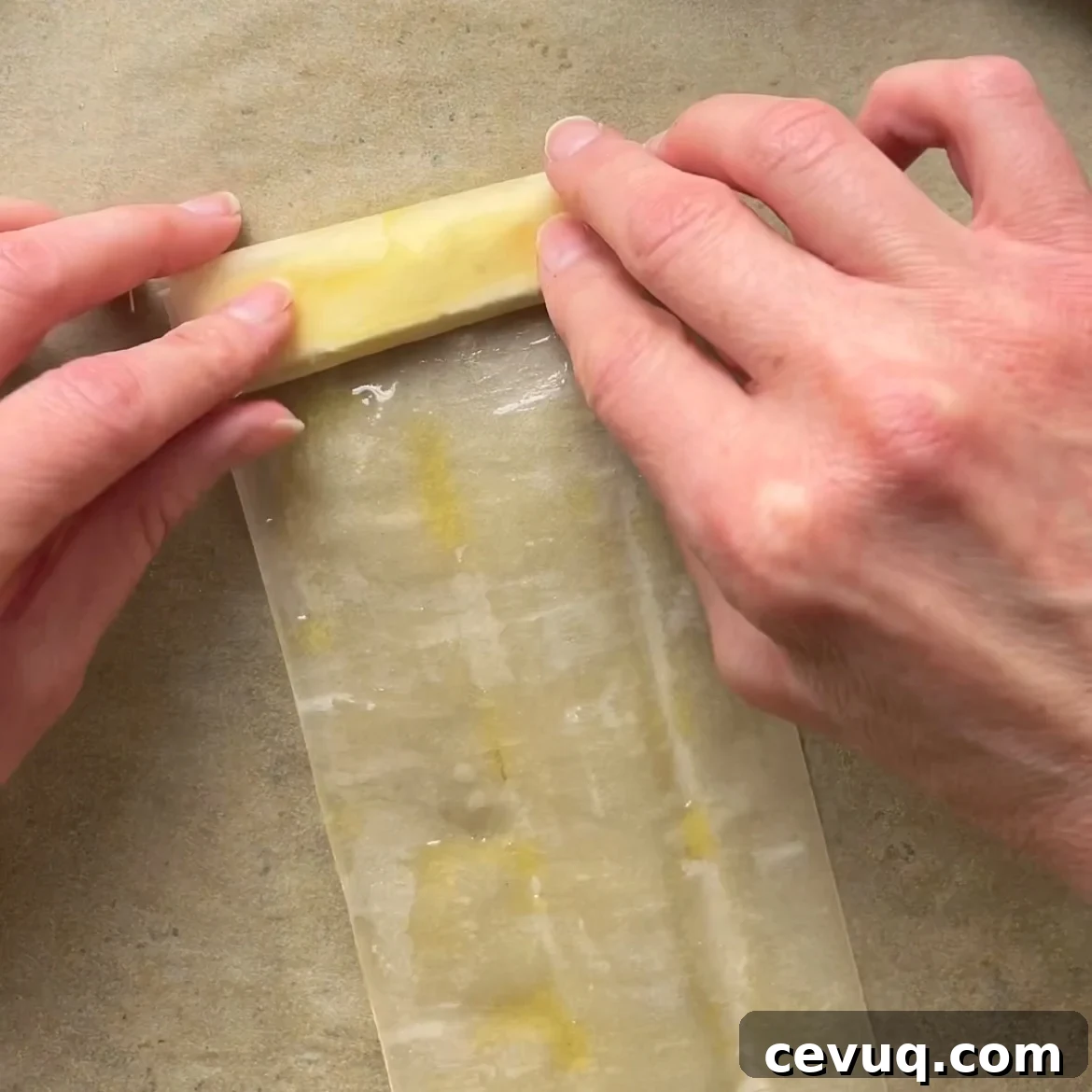 Two hands are rolling a feta slice into a phyllo sheet.