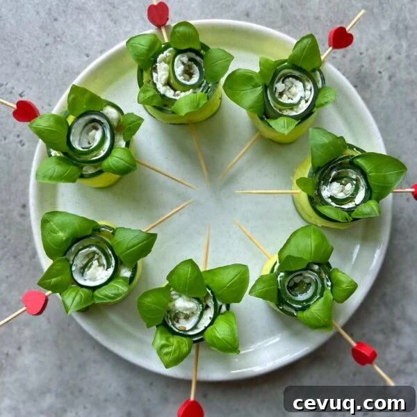 Six cucumber roll ups filled with white cheese and leafy greens are arranged in a circle on a plate, each held together with a wooden skewer topped with a red heart.