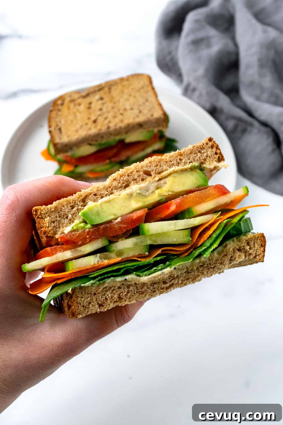 A hand holding a half of a cucumber hummus sandwich with veggie toppings.
