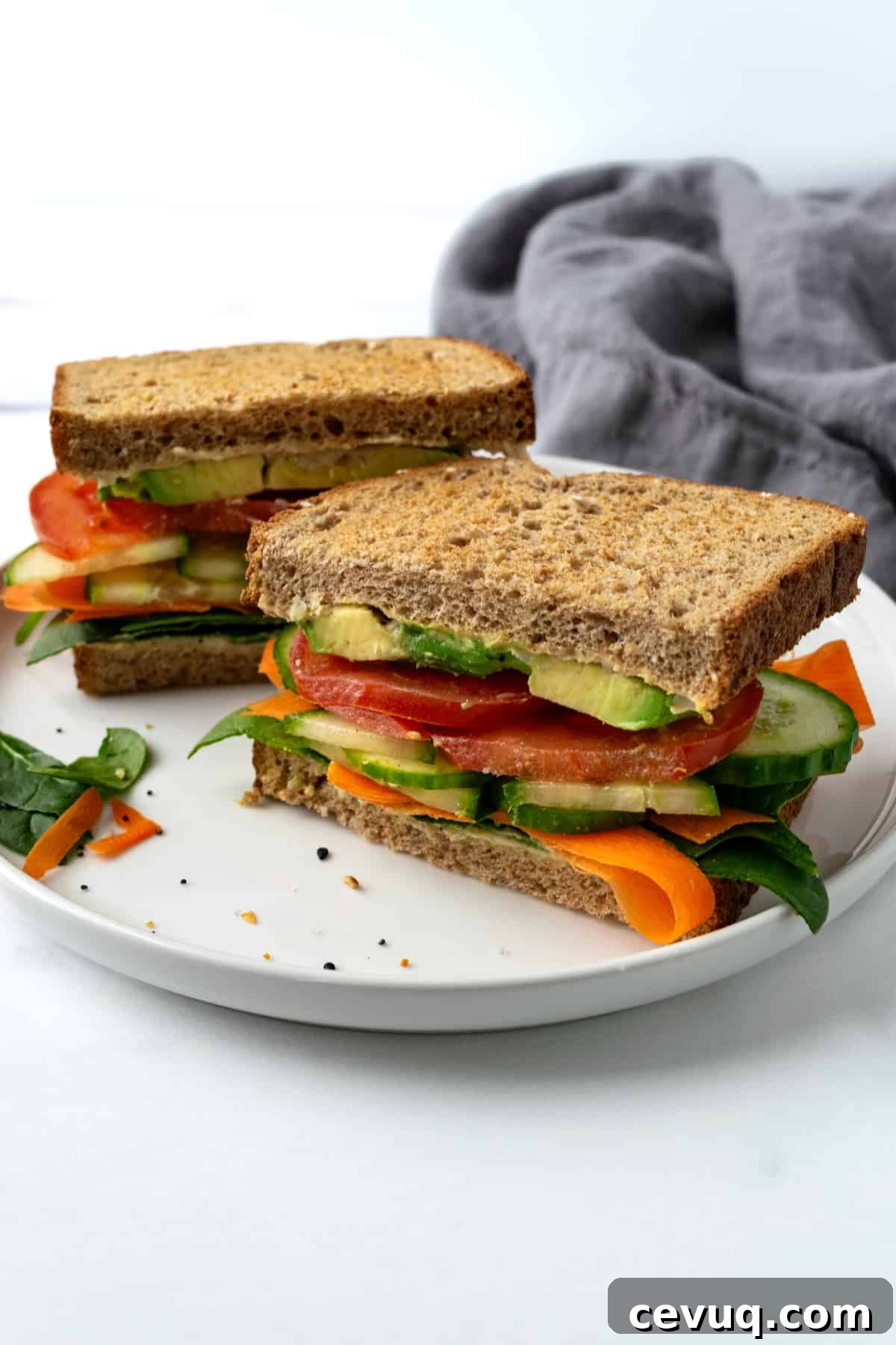 Cucumber Hummus Sandwich cut in half on a white plate.
