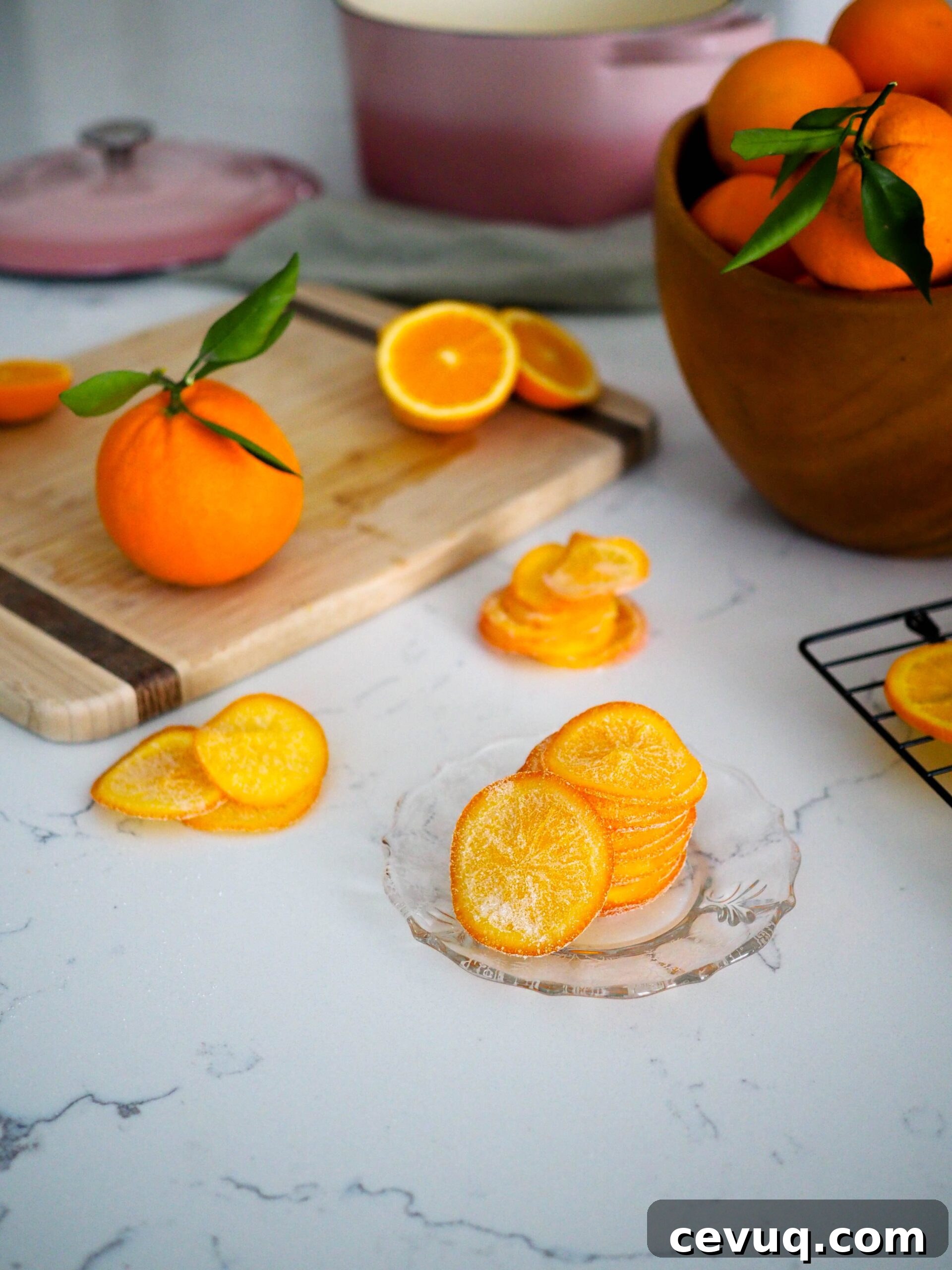 A stack of candied orange slices on a glass plate with styled oranges around it.