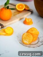 A stack of candied orange slices on a glass plate, with a bowl of oranges in the background.