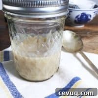 A jelly jar half full of bacon grease on a blue and white napkin