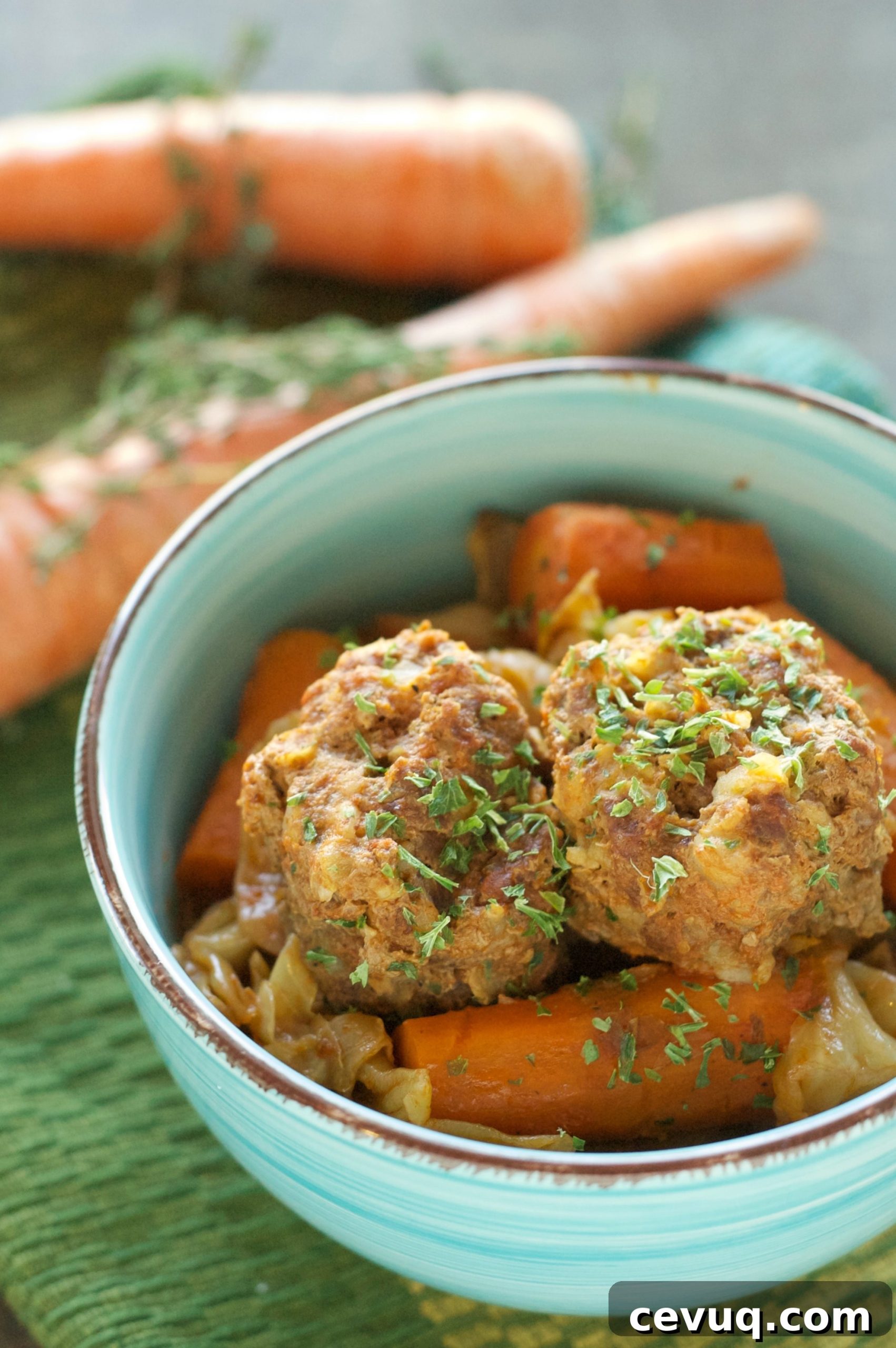 green bowl with two meatballs, carrots and cabbage on green placemat with two carrots in background