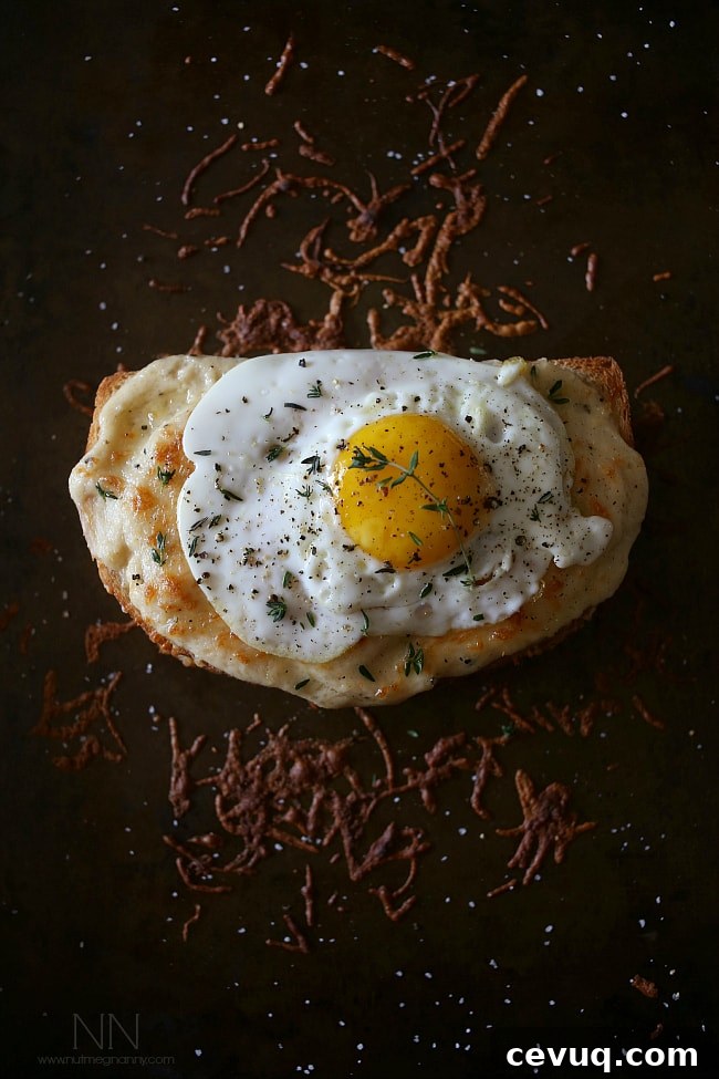 This croque madame is the perfect combination of bechamel cheese sauce, Canadian bacon and Swiss cheese stuffed between two slices of crusty bread and topped with a fried egg. Perfect for breakfast or dinner. Croque Madame on a sheet pan.
