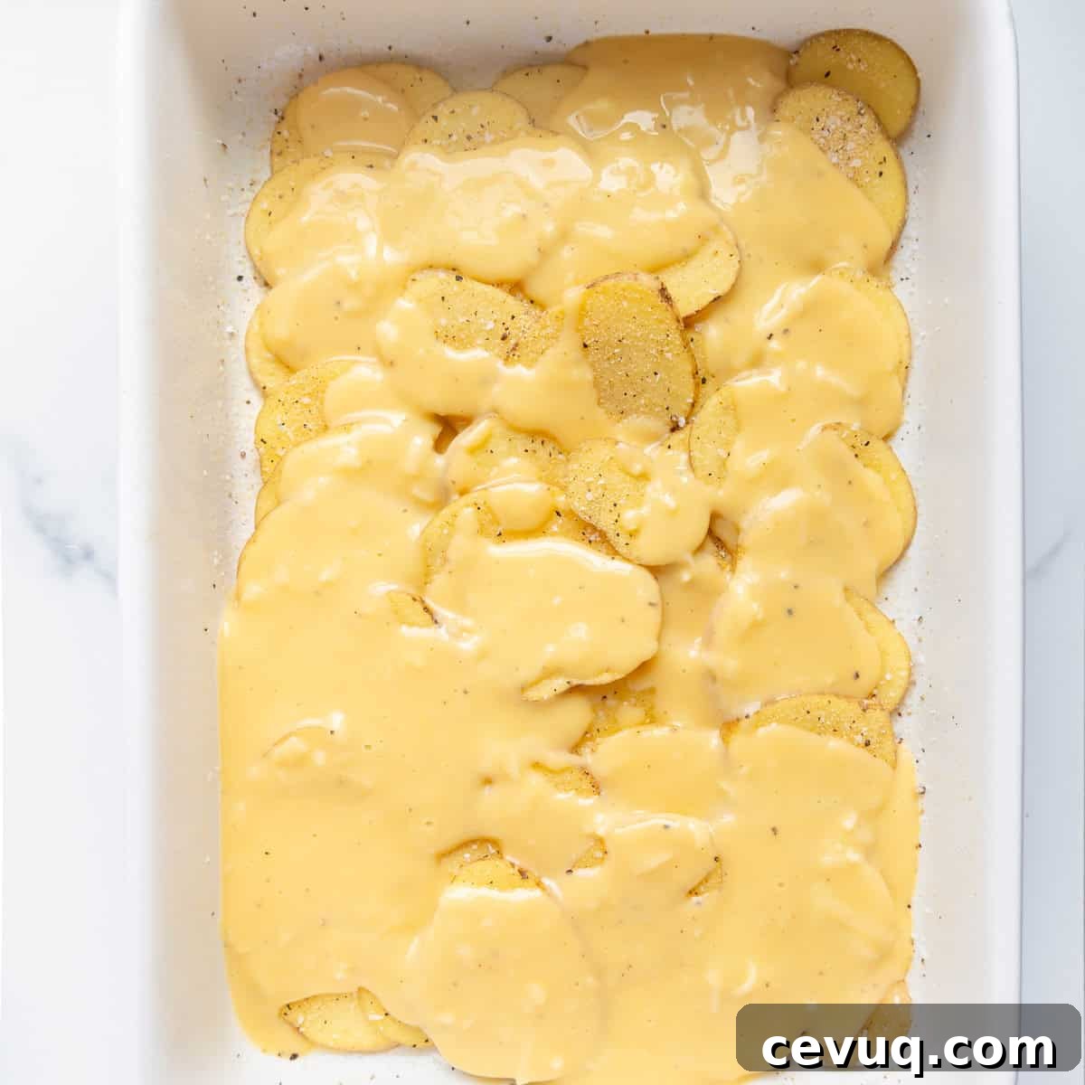 A baking dish filled with potato slices covered in a creamy cheese sauce, ready for baking.