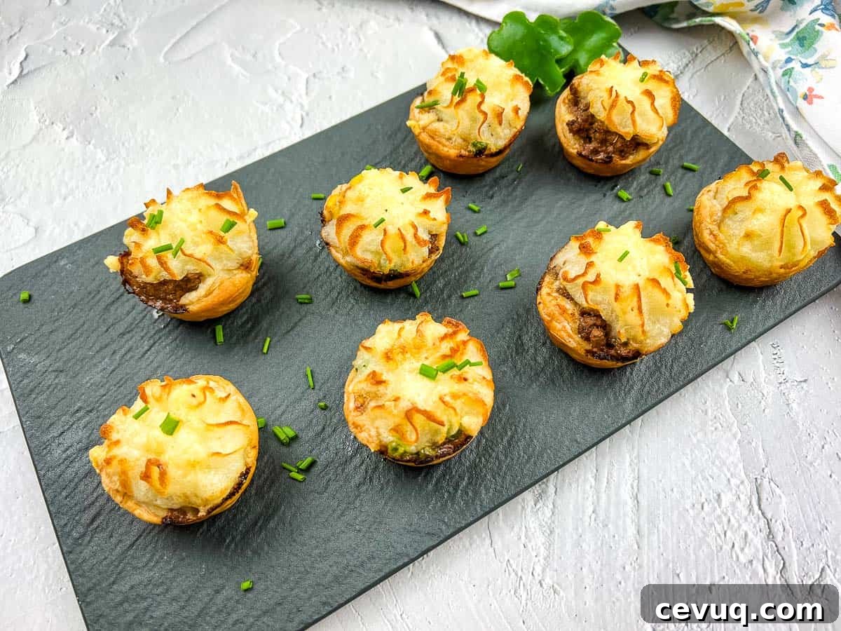 Eight Shepherd's Pie Bites are arranged on a slate board, garnished with chopped chives.