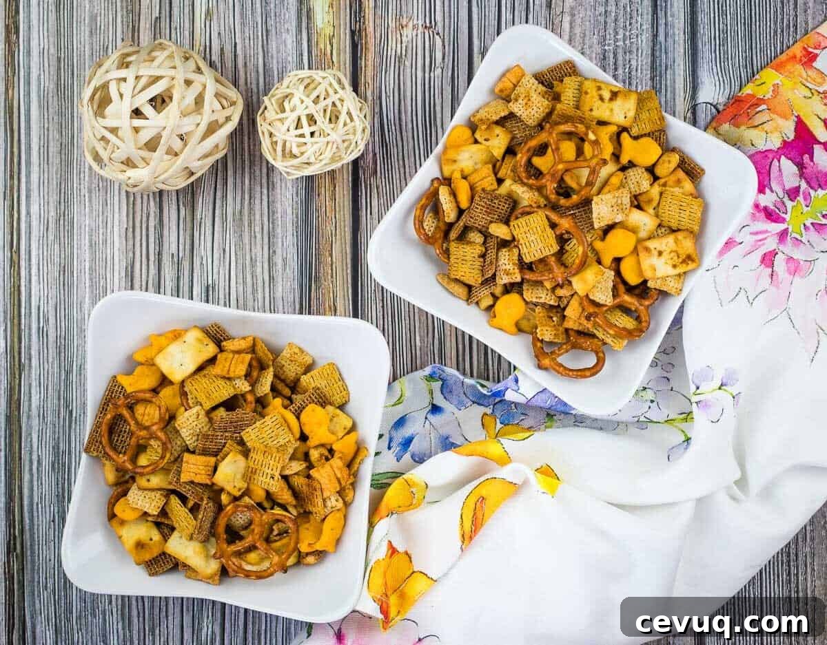 Two bowls of snack mix with pretzels and cereal on a wooden table, accompanied by decorative balls and a colorful napkin.