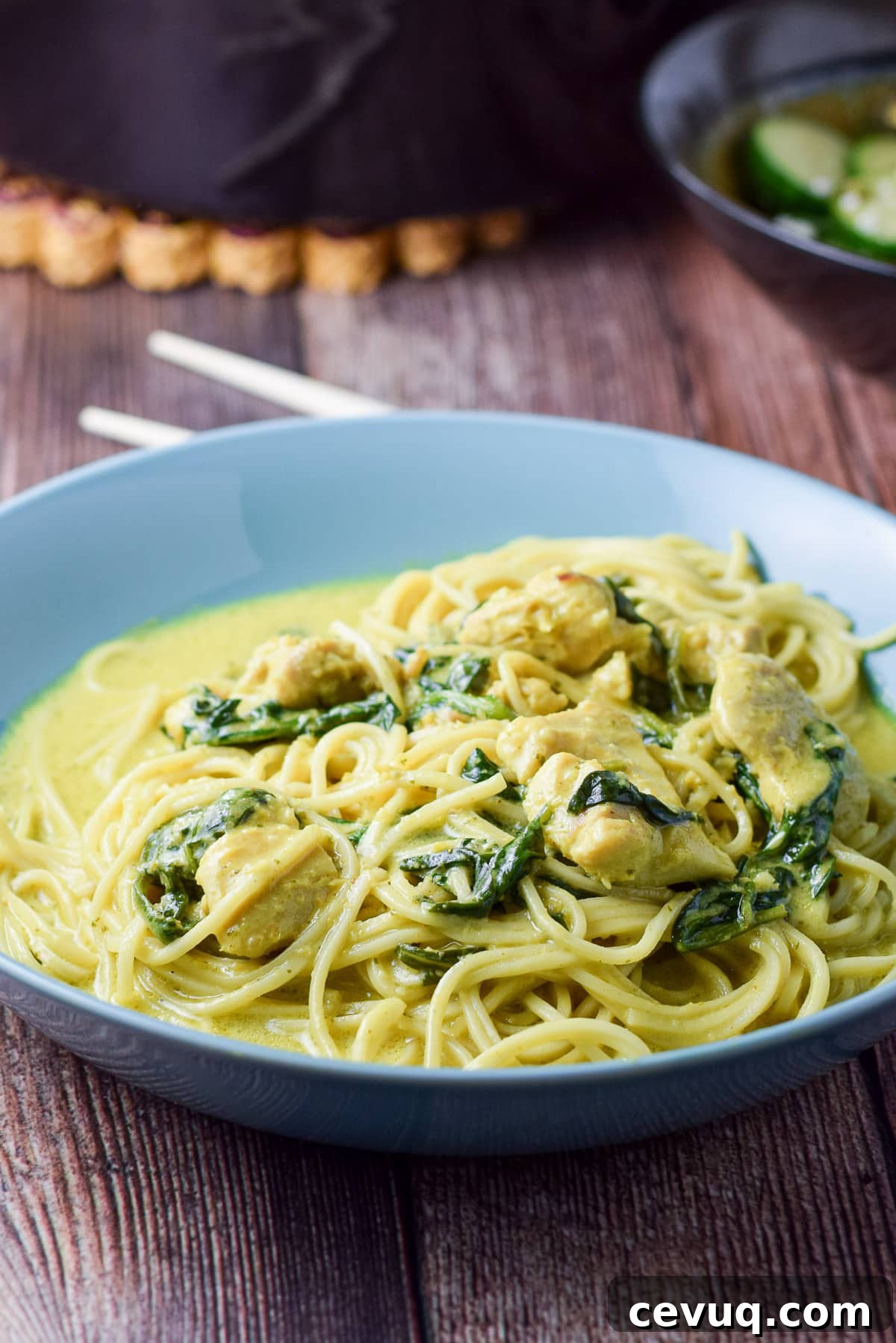 A blue deep dish with noodles, spinach, chicken, and curry sauce