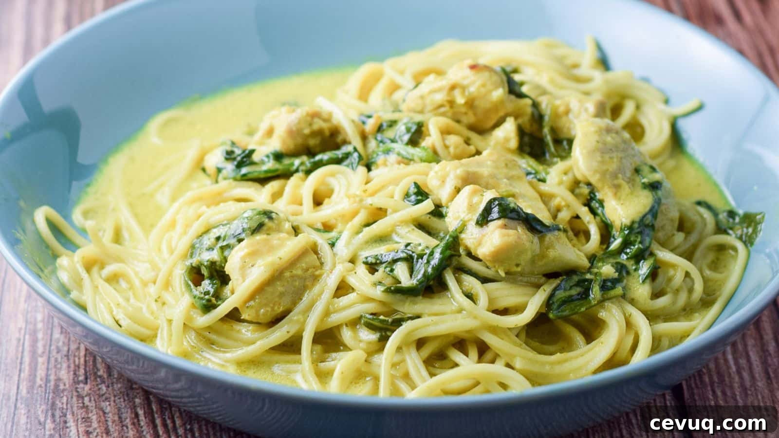 a blue green bowl filled with chicken, spinach, noodles and curry sauce