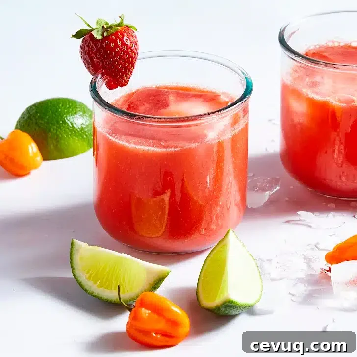 Two glasses of bright red strawberry habanero margarita. The glass is garnished with a strawberry and surrounded by habaneros and lime slices.
