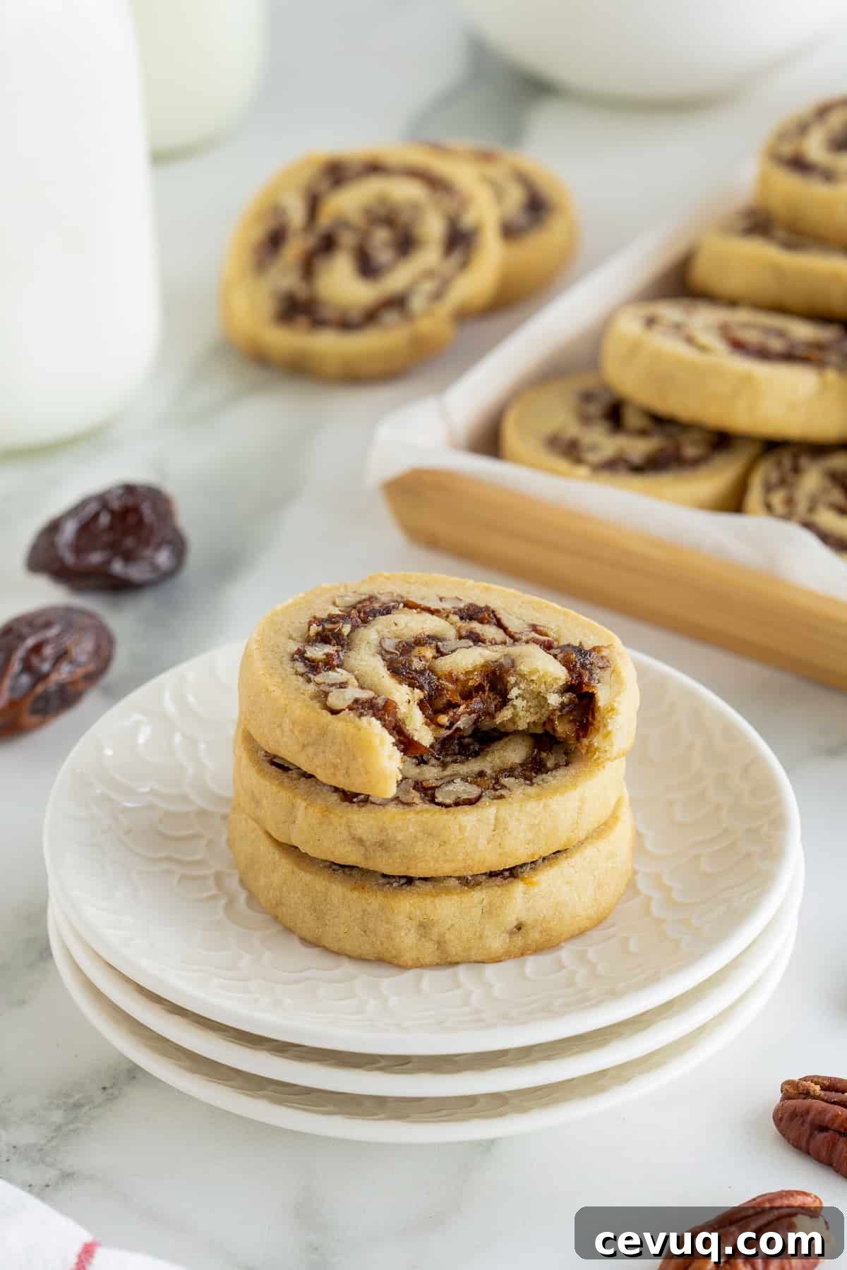 Date Pinwheel Cookies Recipe — Irresistible Swirls of Sweet Date Filling 10 A date pinwheel cookie with a bite missing resting on top of two cookies on a stack of white plates.
