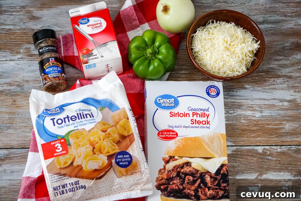 Montreal steak seasoning, heavy whipping cream, a green bell pepper, an onion, shredded provolone cheese, seasoned Sirloin Philly Steak, and a bag of frozen Cheese Tortellini on a red and white checked handkerchief.