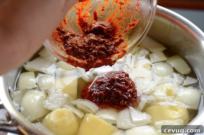 Spicy seasoning is added to potato and onion in a pot.