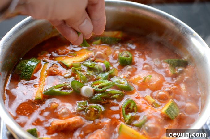 Chopped green onion is sprinkled on spicy tuna potato stew in a pot.