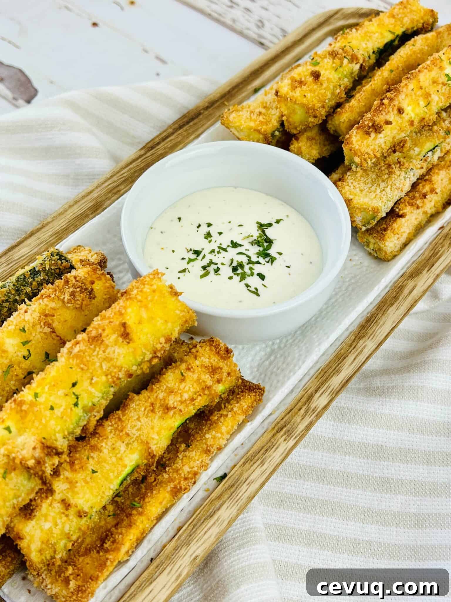 A wooden tray with the zucchini sticks and a bowl of dipping sauce in the middle.