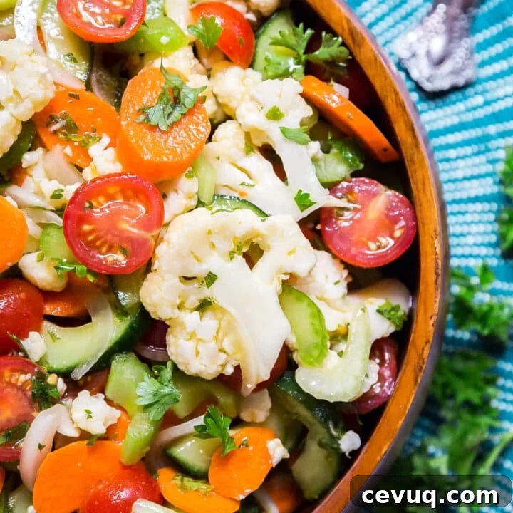 An overhead image of one side of a bowl of vegetable salad on a blue placemat.