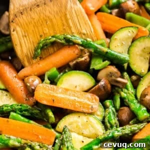 A close up image of sautéed veggies in a pan with a wooden turner in it.