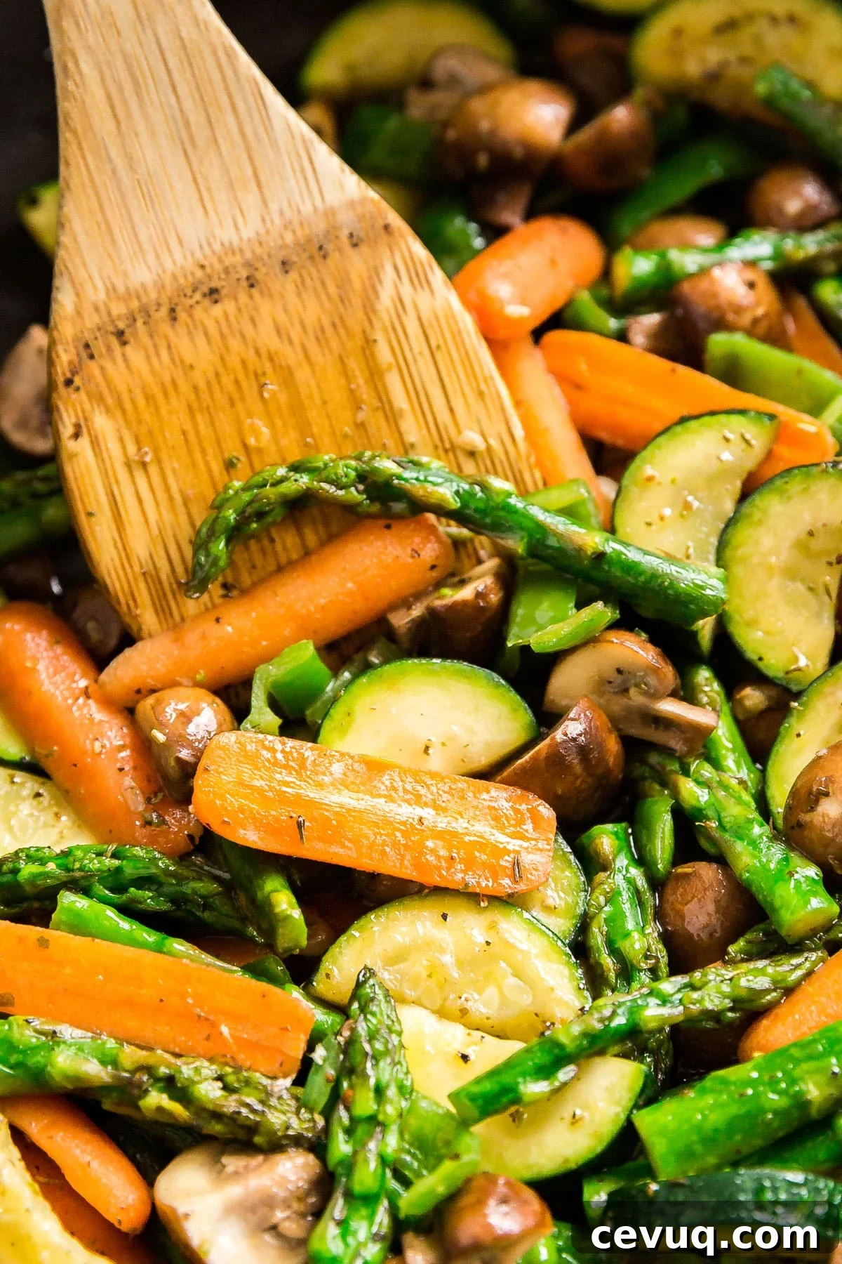 A close up image of sautéed veggies in a pan with a wooden turner in it.