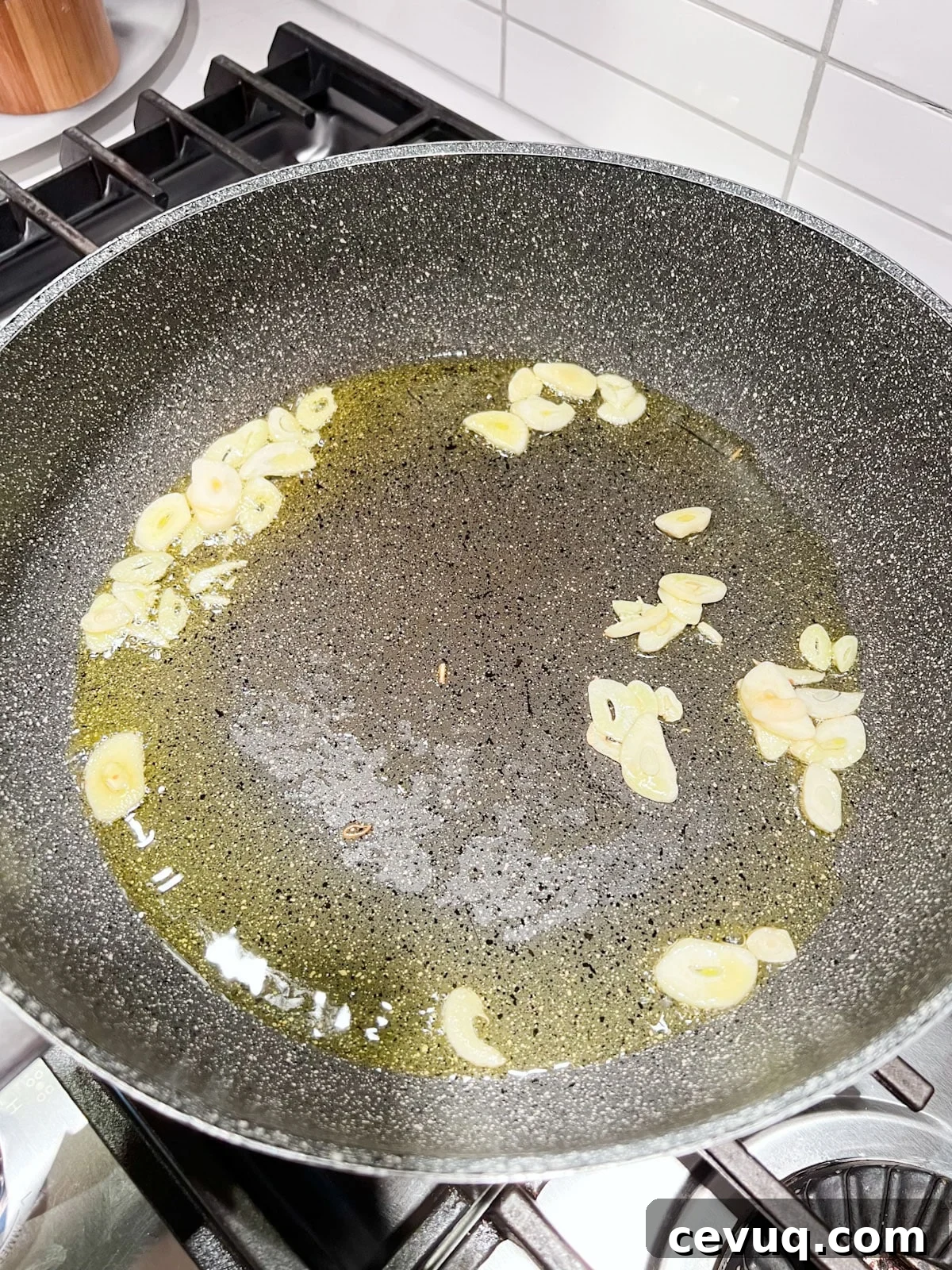 A sauté pan with hot oil and sliced garlic in it.