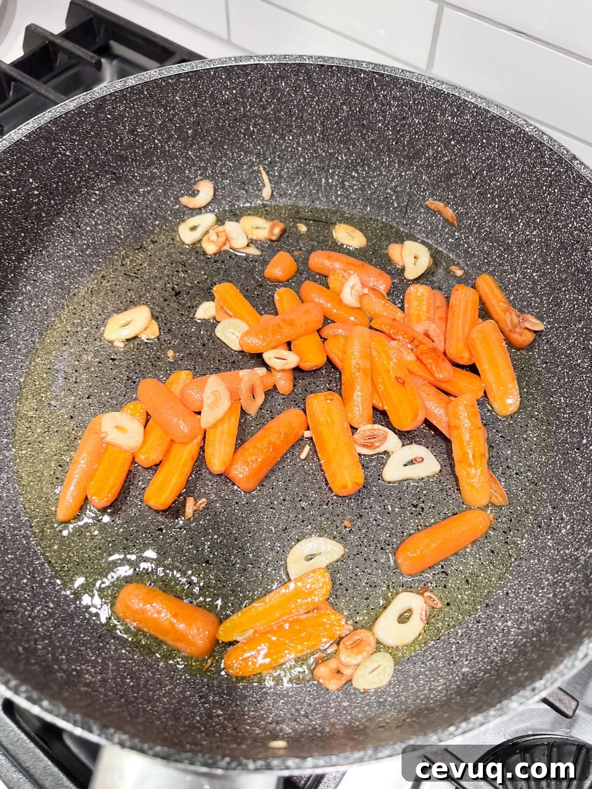 A sauté pan with carrots added to the hot oil and sliced garlic in it.