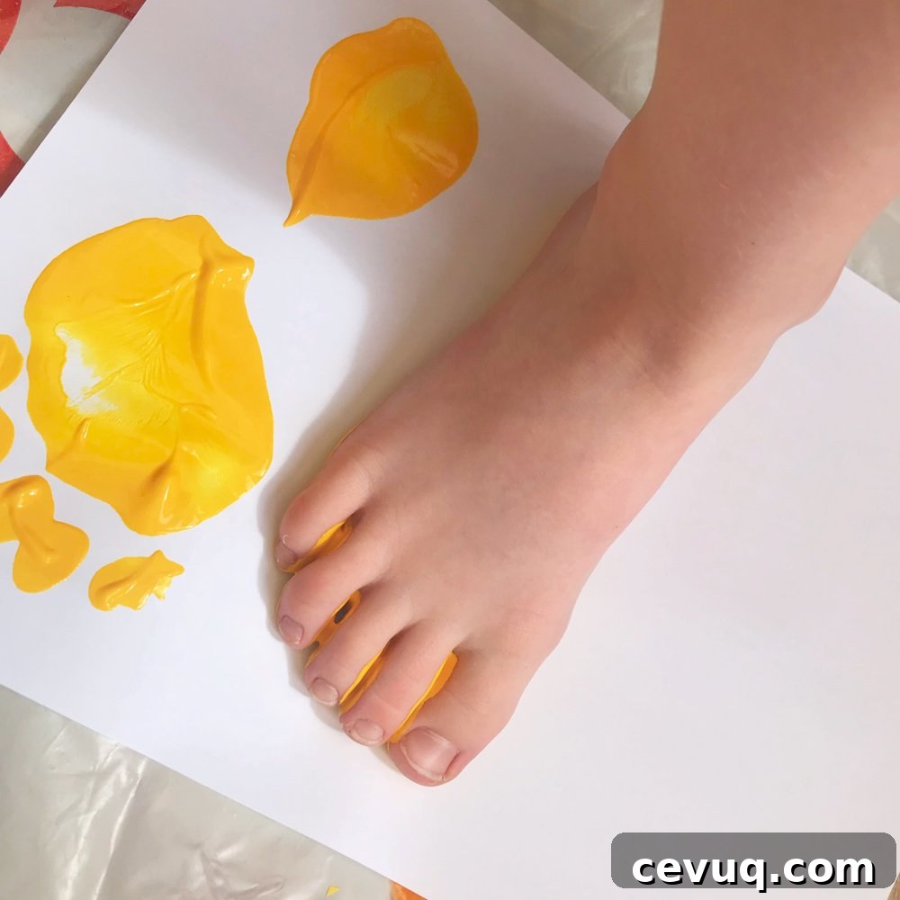 small child making painted footprints with yellow paint