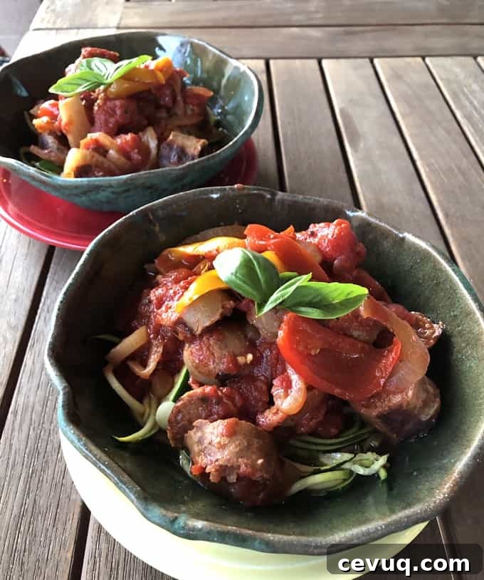 Sausage and peppers over zucchini noodles topped with fresh basil in decorative ceramic bowls.