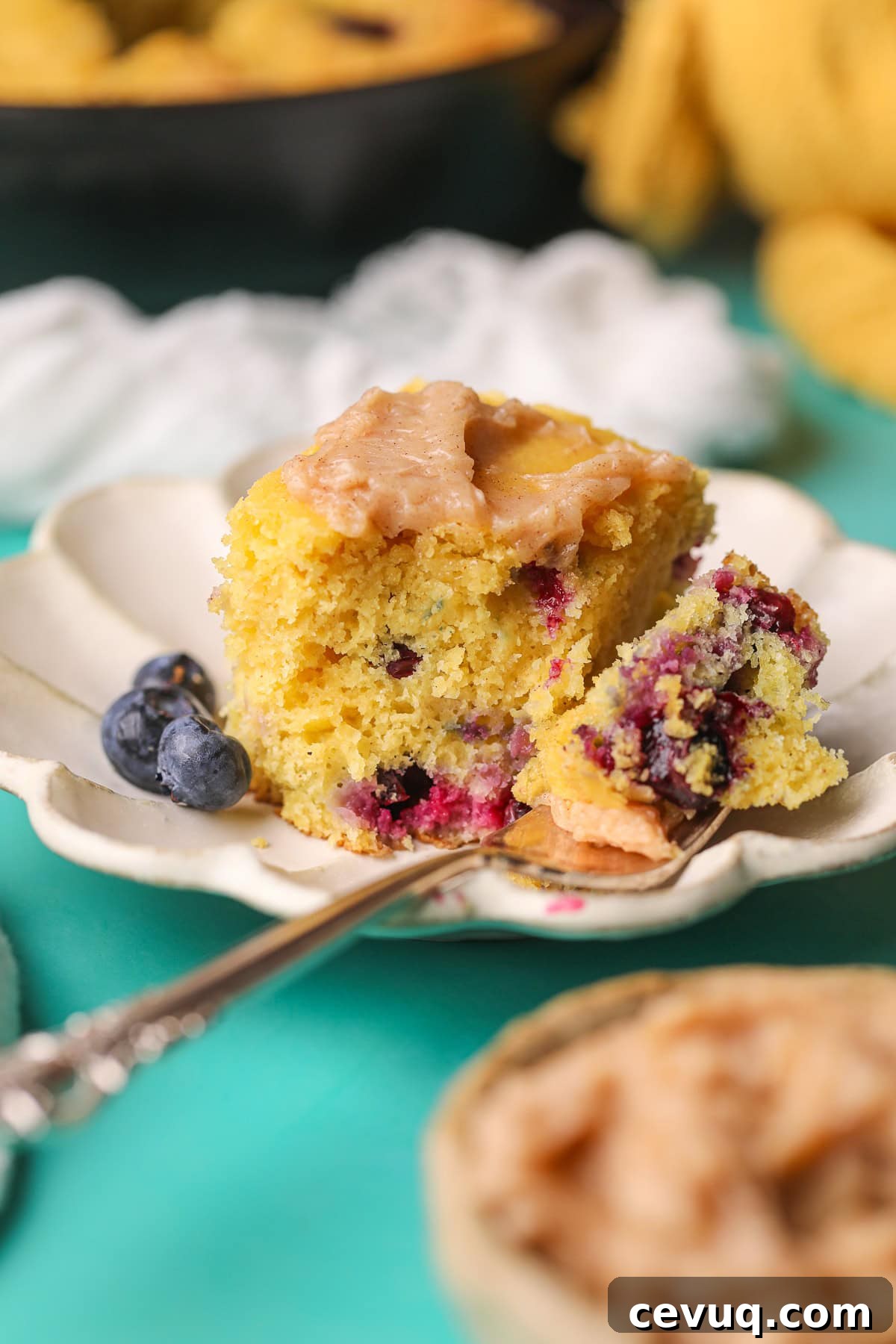 A slice of blueberry cornbread with cinnamon honey butter on a white plate.