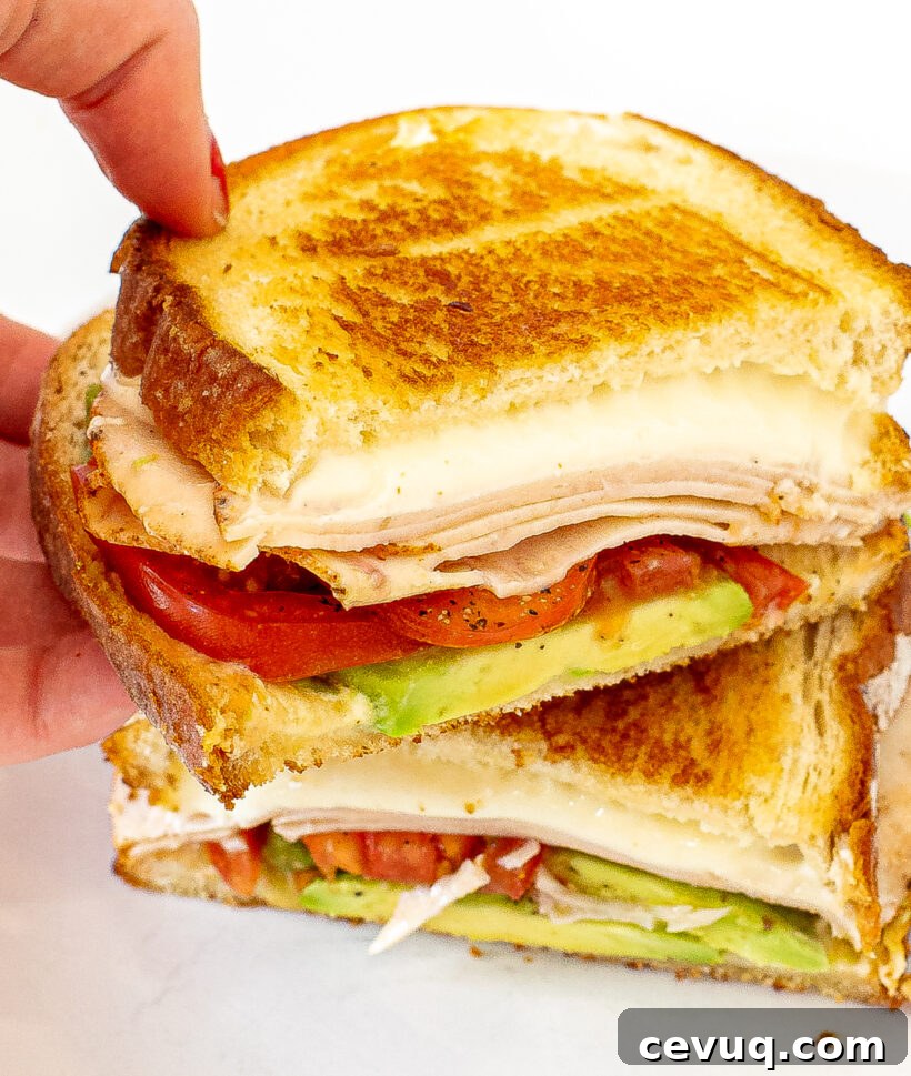 Hand holding half of a California grilled cheese with the other half on a plate. 