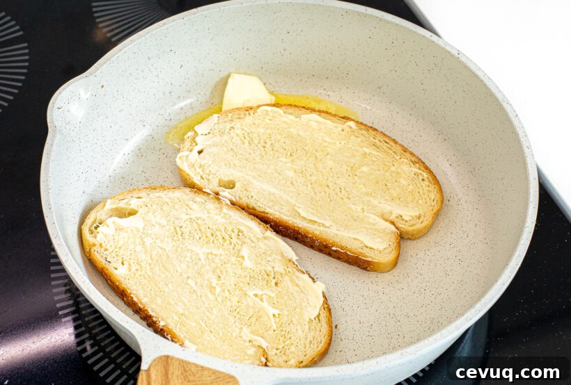 Two slices of bread in a pan spread with mayonnaise on top. 