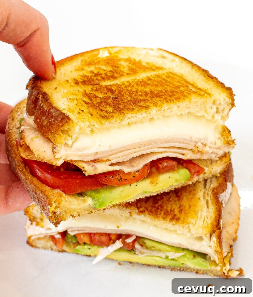 Hand holding a half of a California grilled cheese to show the layer inside with the other half on a plate. 