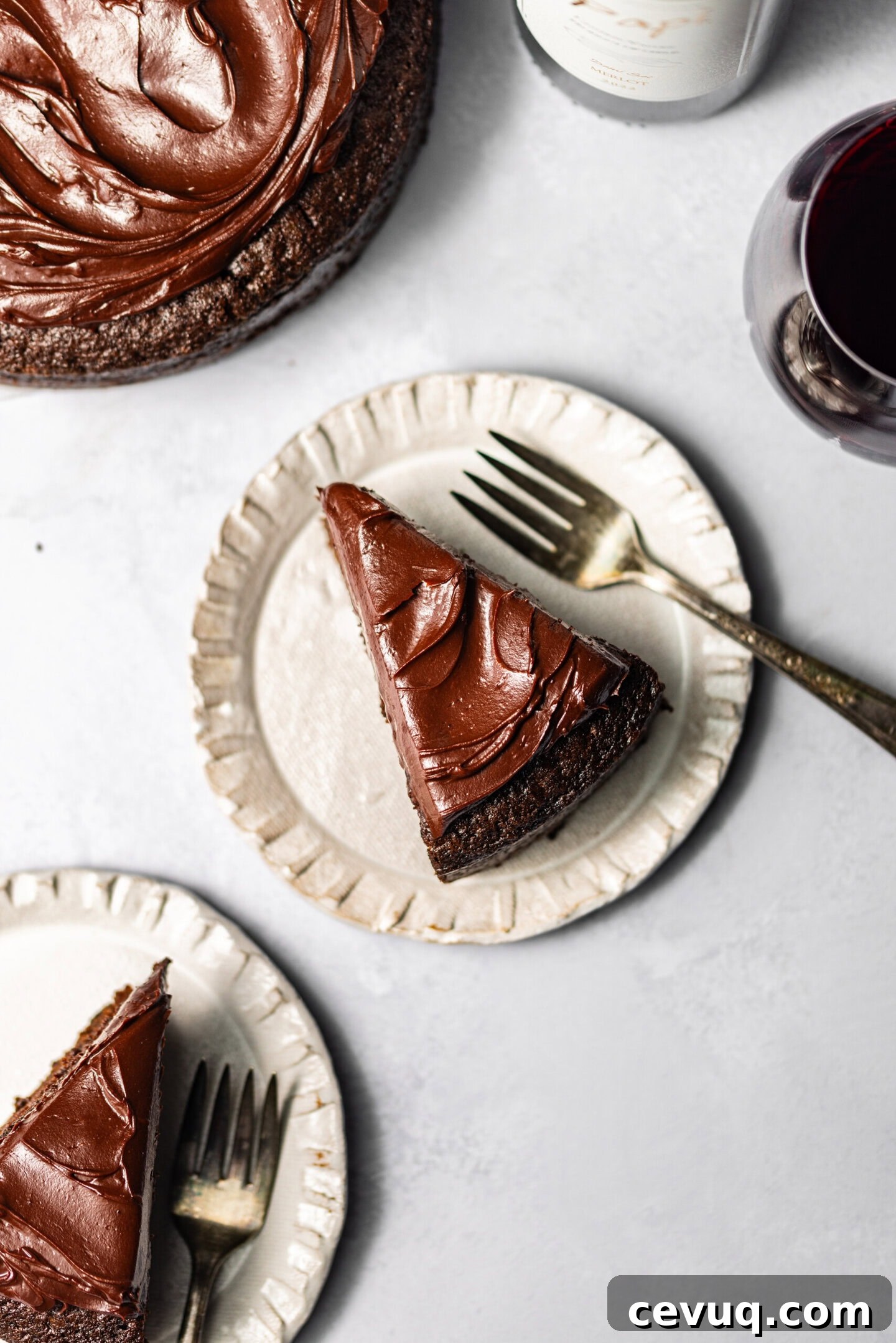 Slices of red wine chocolate cake with chocolate ganache on top on plates with forks next to each slice and a wine glass nearby.