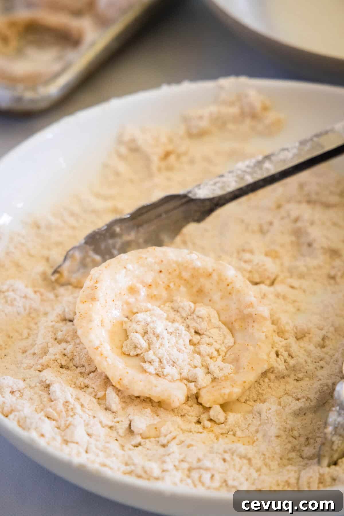breading onion ring in bowl of flour