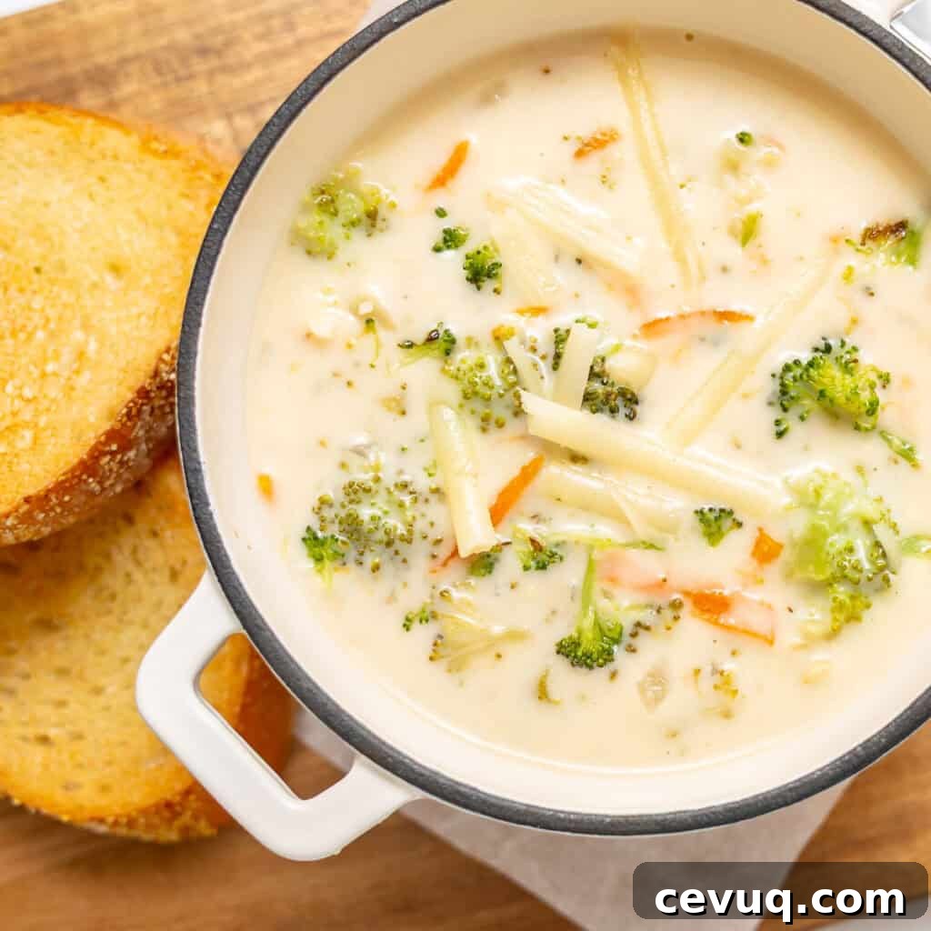 A pot of creamy broccoli and cheese soup with visible carrot and broccoli pieces, next to two slices of toasted bread on a wooden surface.