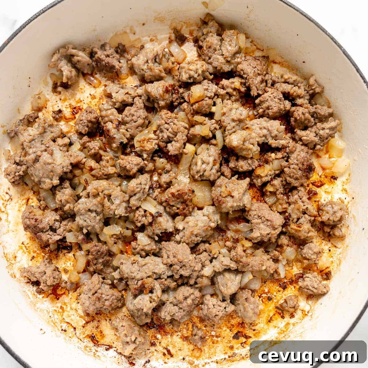Cooked ground meat and diced onions in a white pot, with browned bits and oil visible on the surface.
