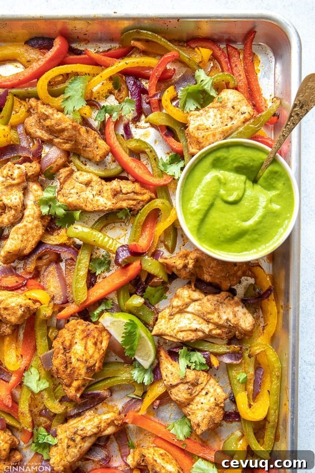 overhead shot of a sheet pan with low carb healthy oven baked chicken fajitas with a side dish containing creamy avocado sauce